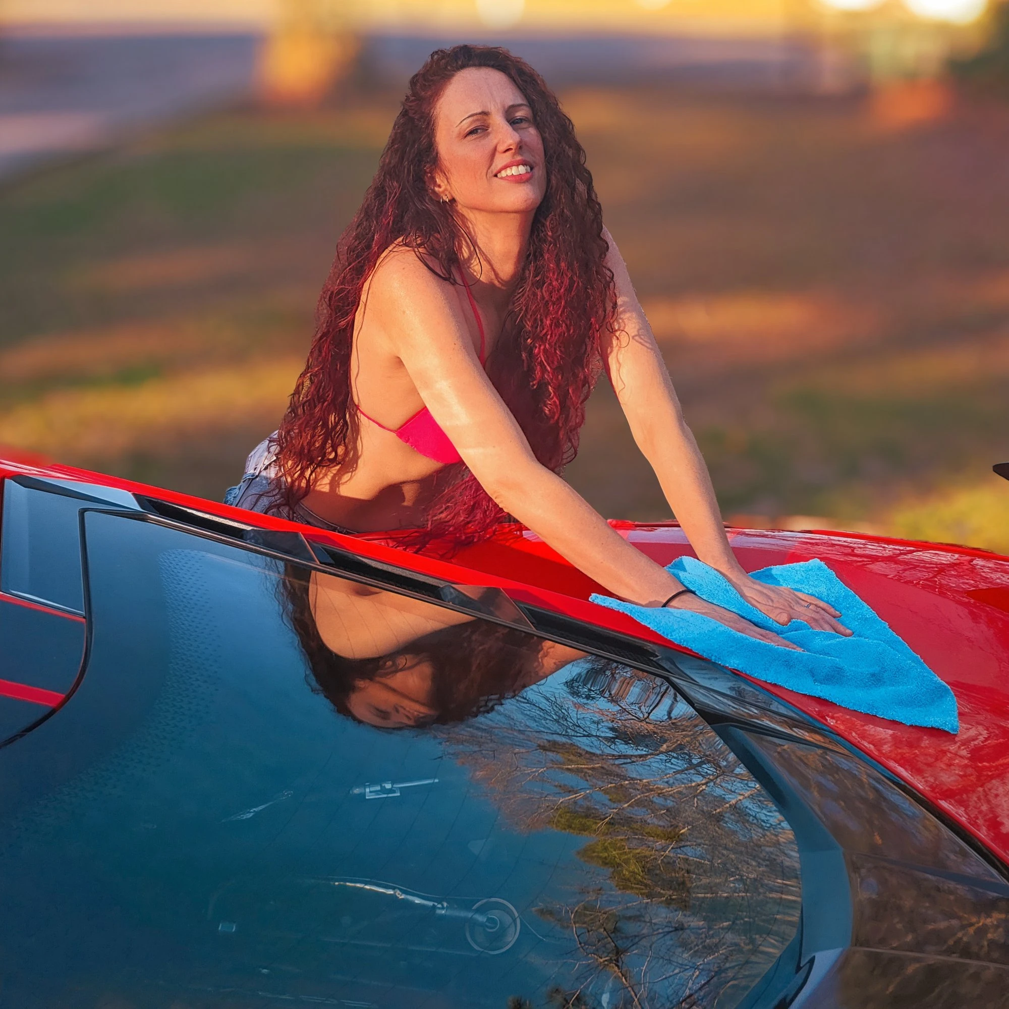 Alice Seal smiling while detailing a Torch Red Corvette during golden hour