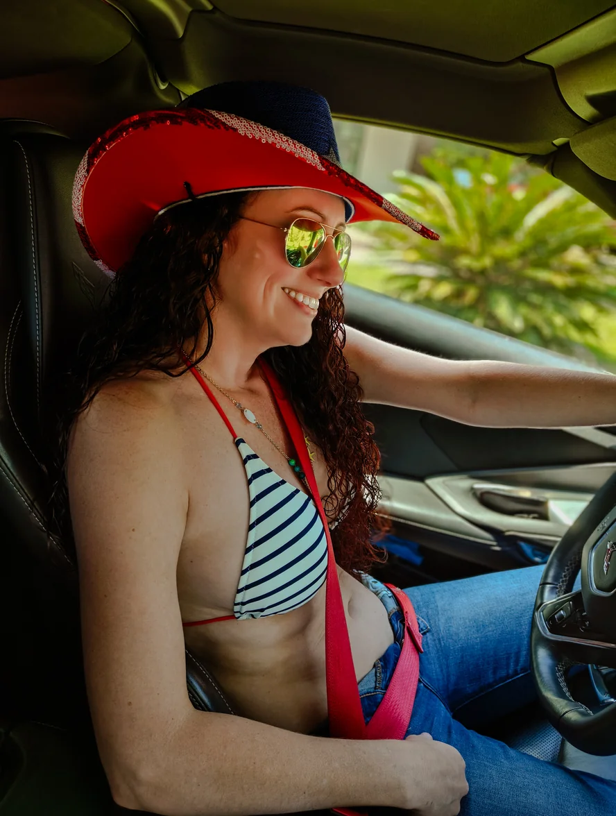 Alice Seal smiling behind the wheel of her Torch Red Corvette Stingray, wearing mirrored aviators and a red, white, and blue cowboy hat